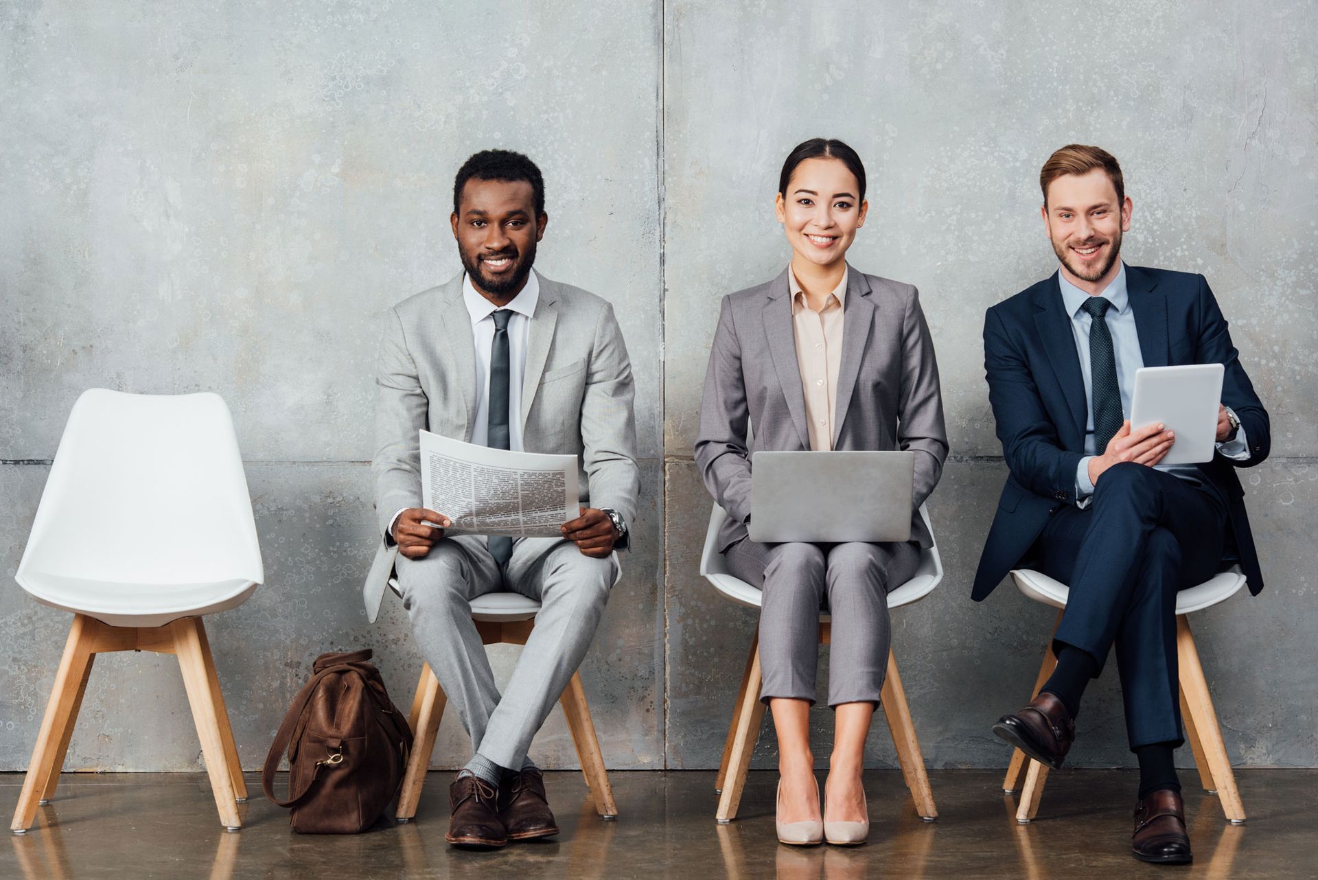 Three diverse professionals seated on chairs, waiting, smiling.
