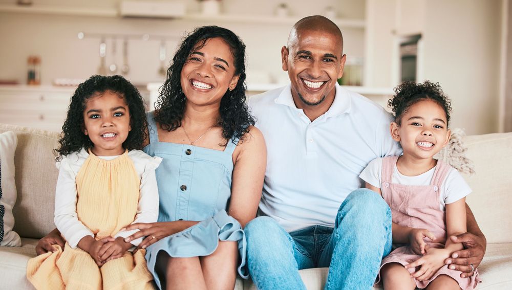 Family of four smiling on a couch: two young girls, a woman, and a man.