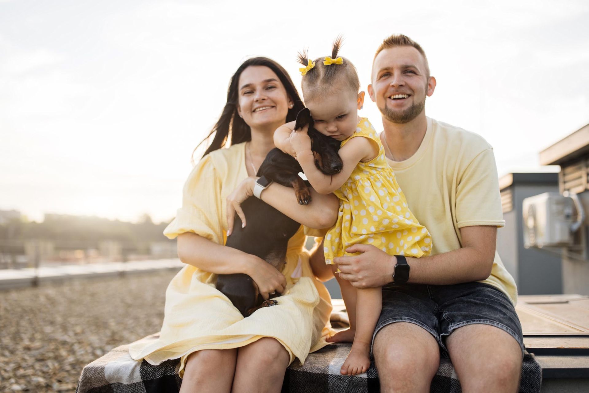 Family of three, including a small child, and a dog sitting on a rooftop smiling; all are wearing yellow.