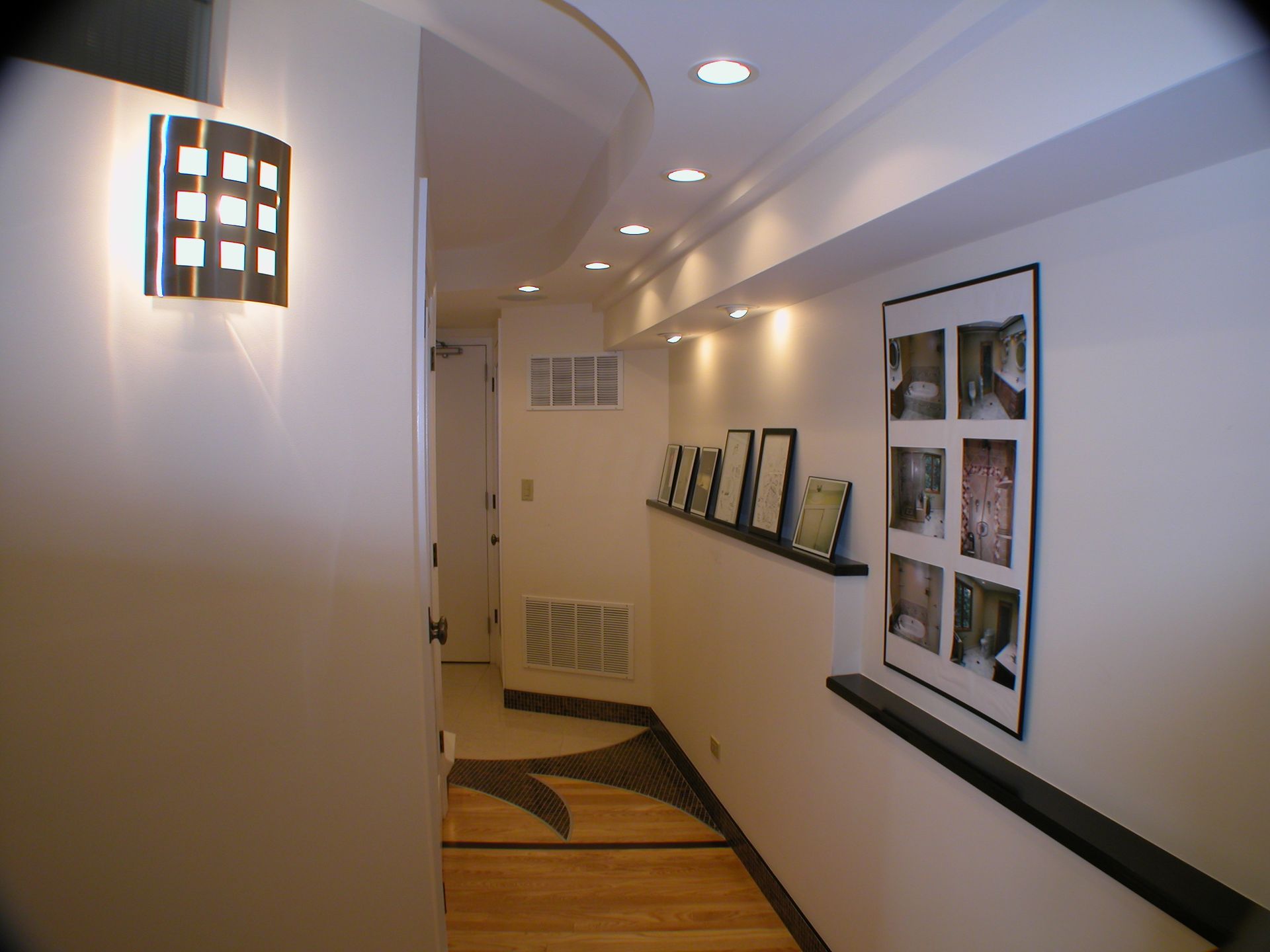 A hallway with pictures on the wall and a lamp on the wall