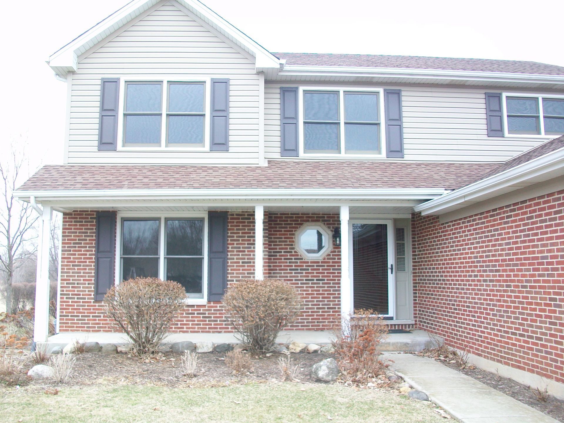 A brick house with a white siding and black shutters