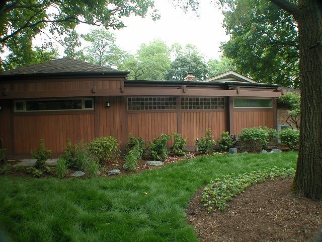 A house with a wooden garage door and a tree in front of it