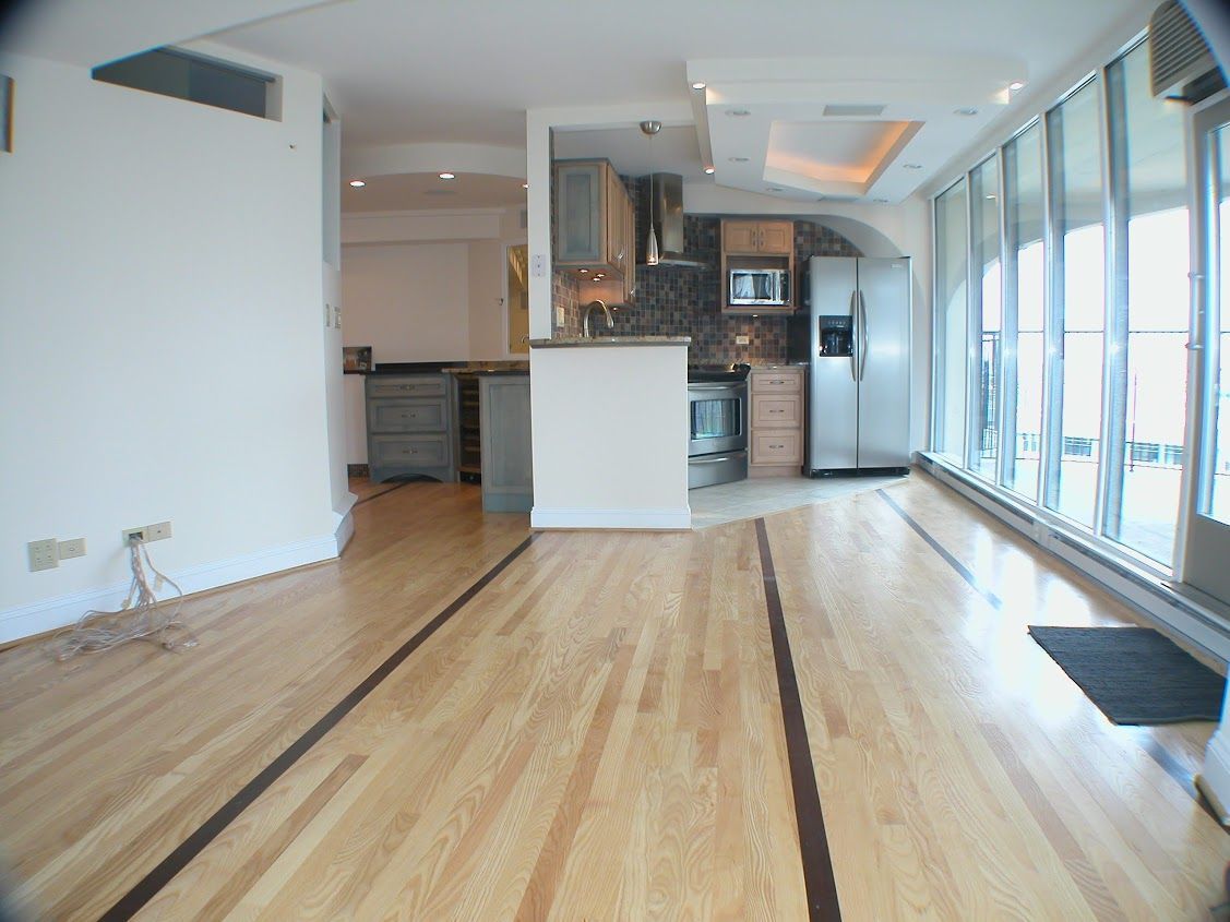 An empty room with hardwood floors and a kitchen in the background