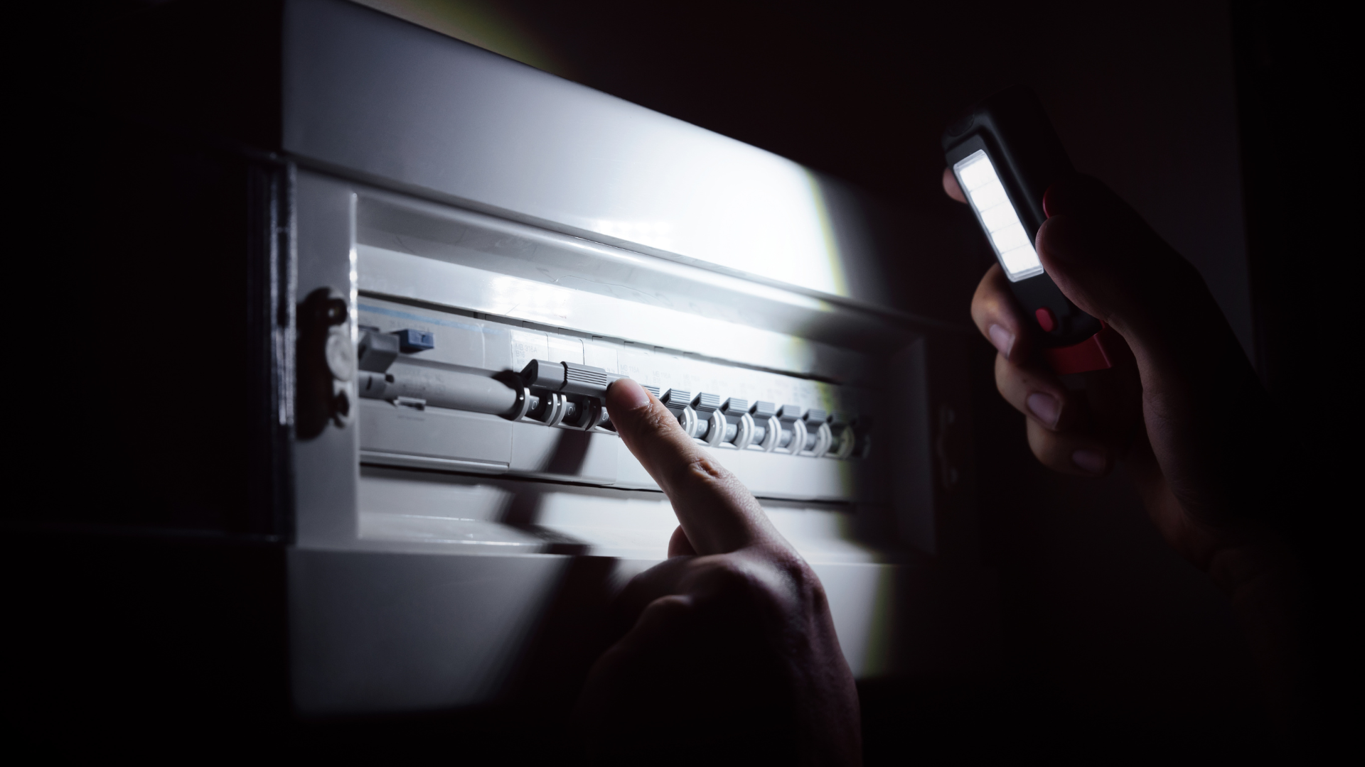 Persona illumina il quadro elettrico con una torcia durante un blackout per controllare i salvavita.