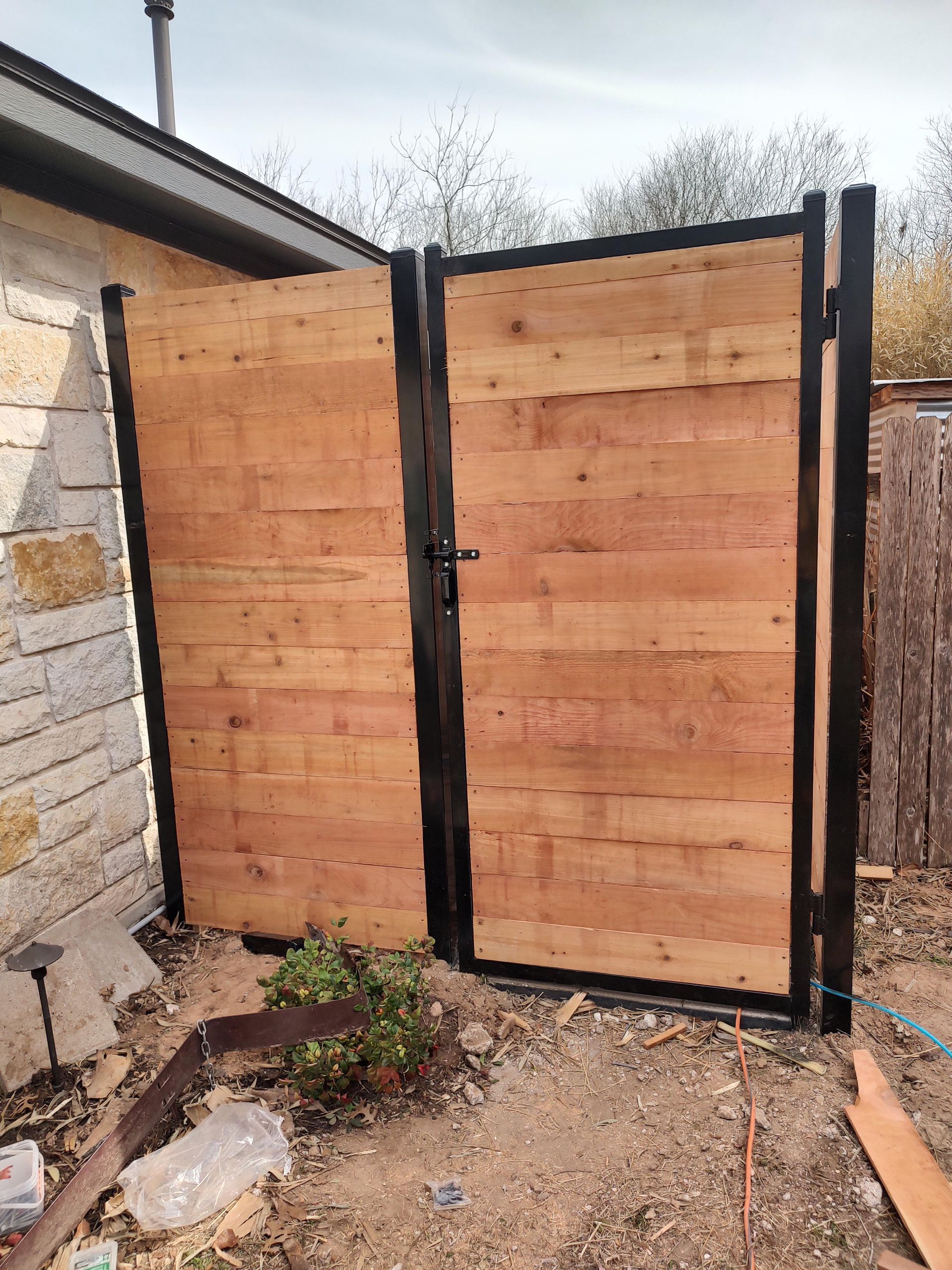 A wooden fence with a metal gate is sitting in front of a house.