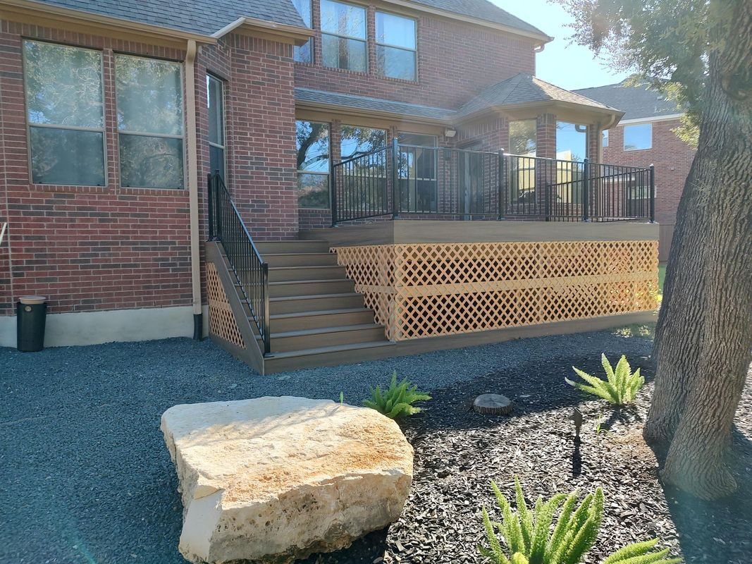 A large rock is in front of a brick house with a deck.
