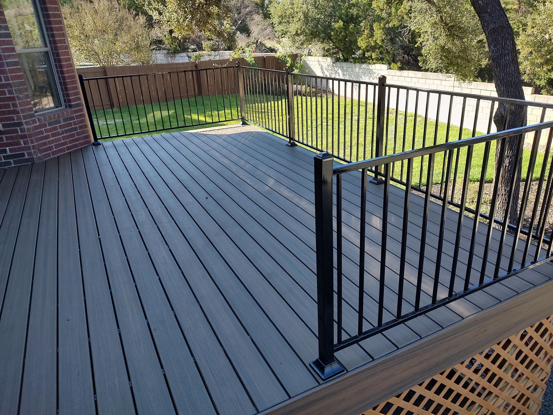 A composite deck with a metal railing and a brick building in the background.