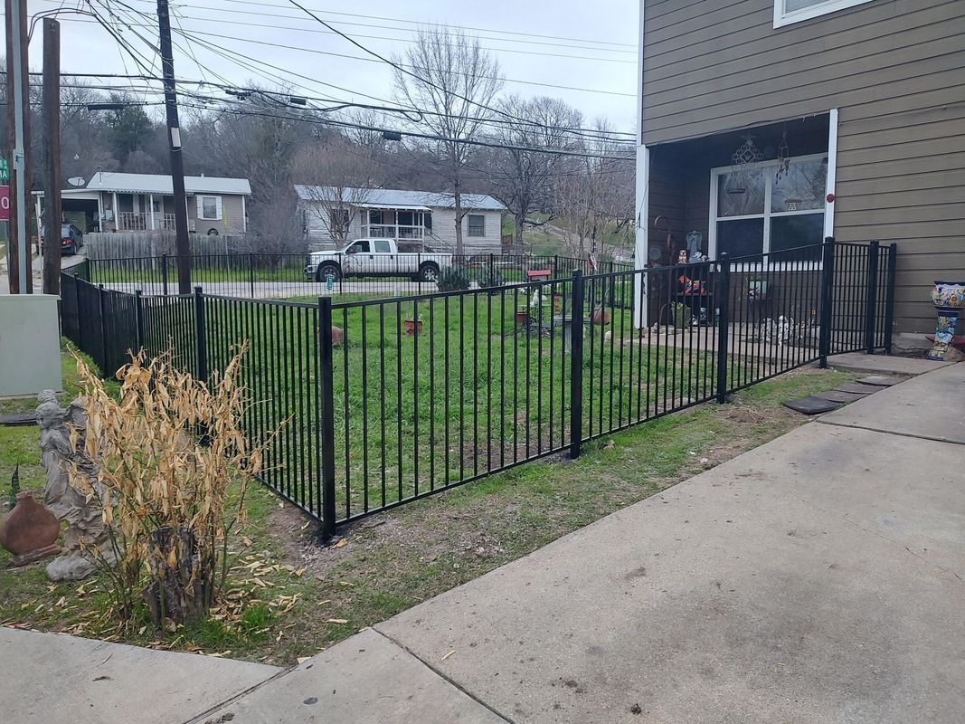 A wrought iron fence is surrounding a yard in front of a house.
