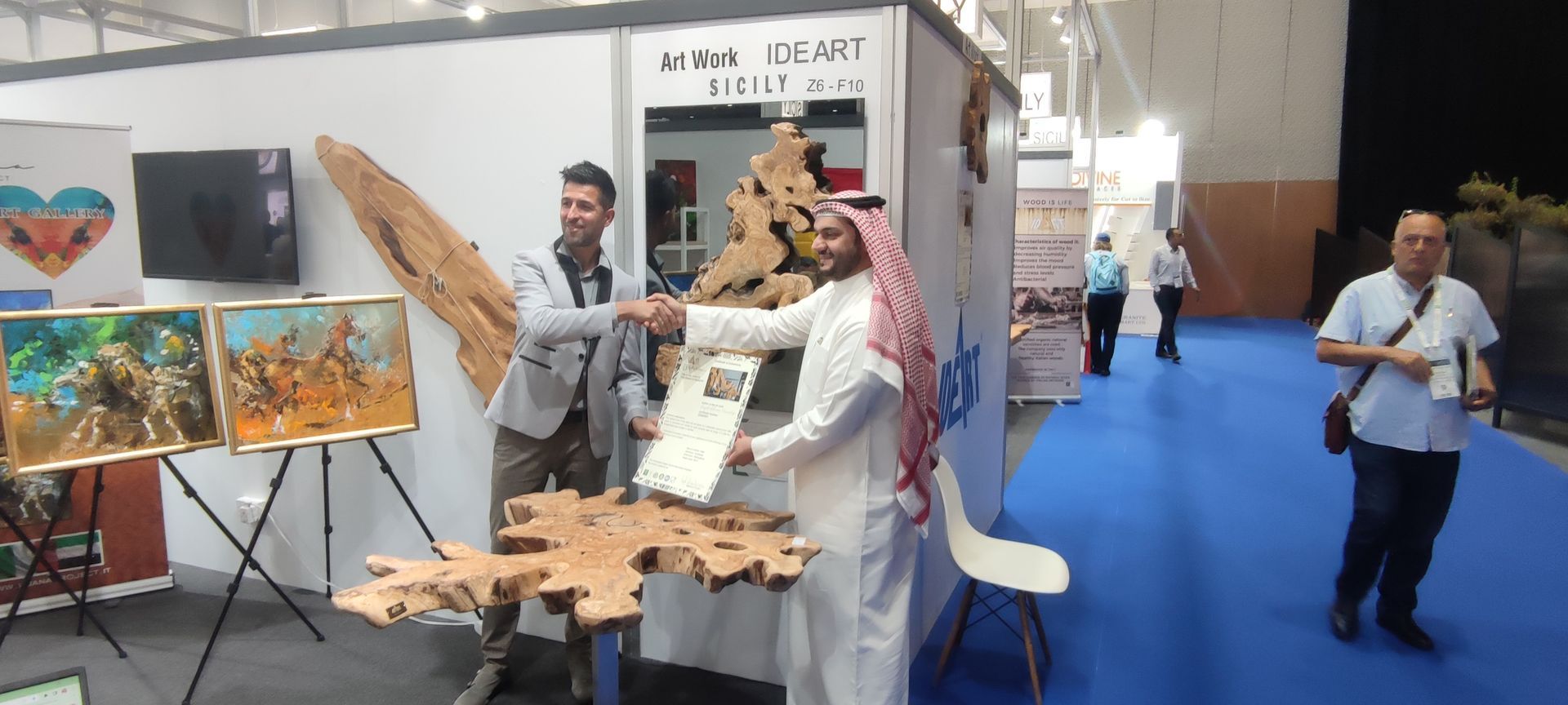 Due uomini si stringono la mano in uno stand di una fiera. Uno indossa abiti tradizionali arabi. L'altro indossa una giacca.