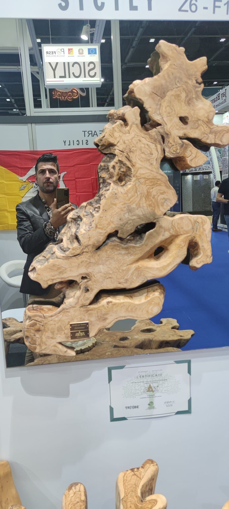 Uomo che scatta una foto a una grande scultura in legno alla mostra sulla Sicilia.