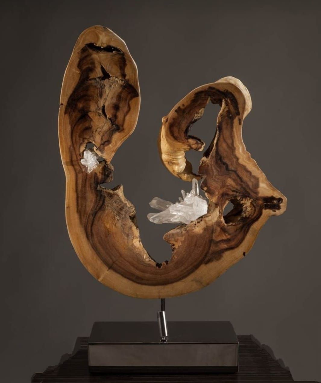 Scultura in legno con cristalli di quarzo su base metallica. Il legno marrone e beige è modellato organicamente con fori.
