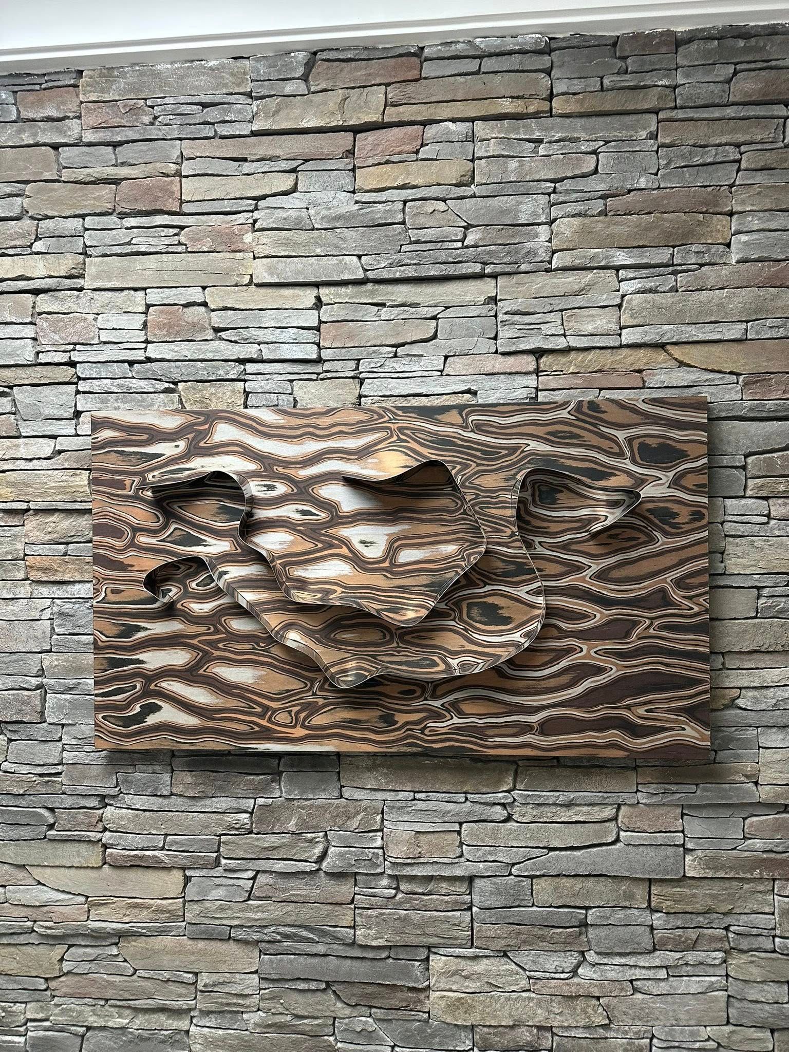 Opera d'arte in legno con forme ritagliate, montata su una parete di pietra.