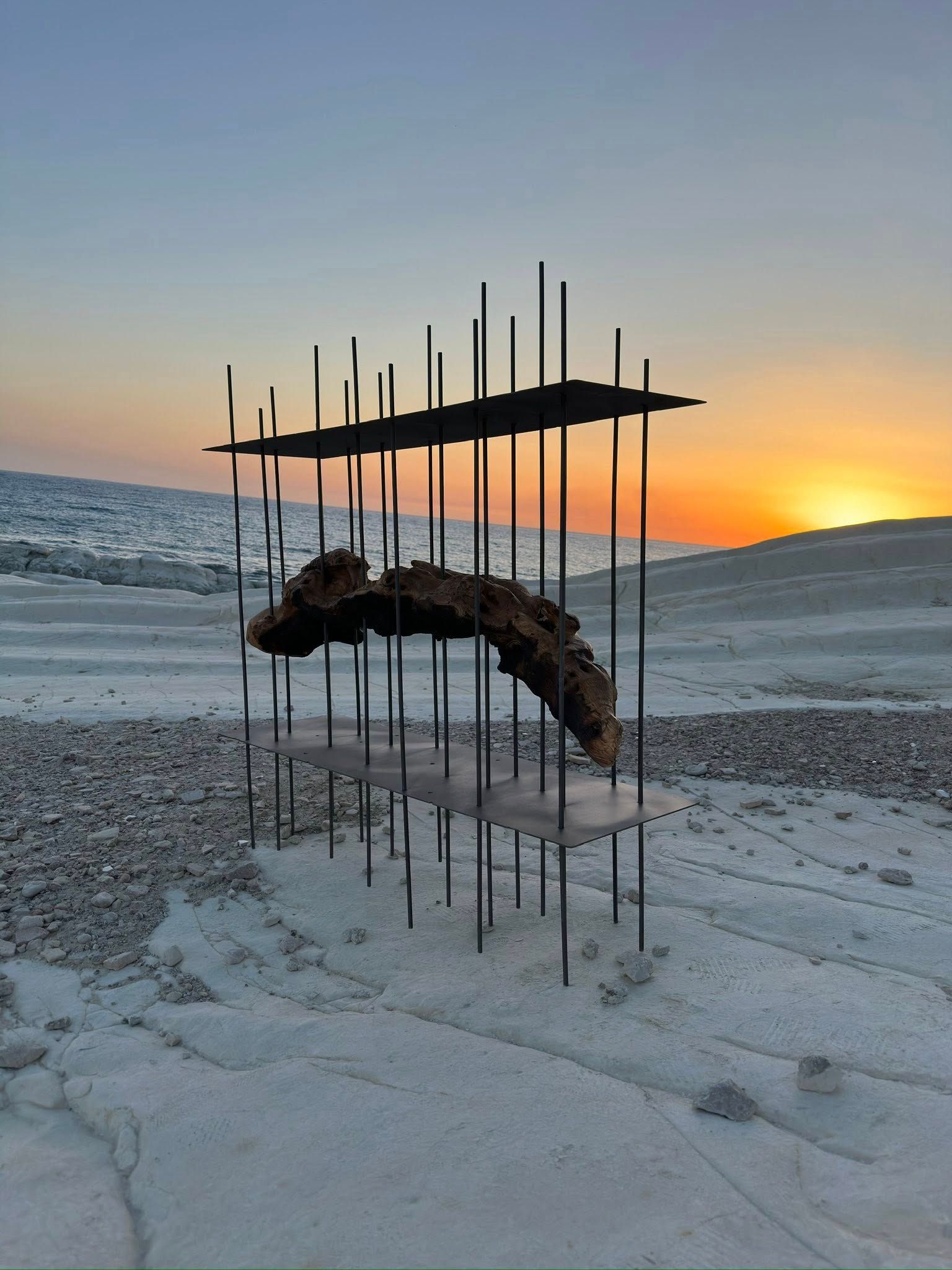 Scultura astratta in metallo su un paesaggio innevato con un tramonto sullo sfondo.