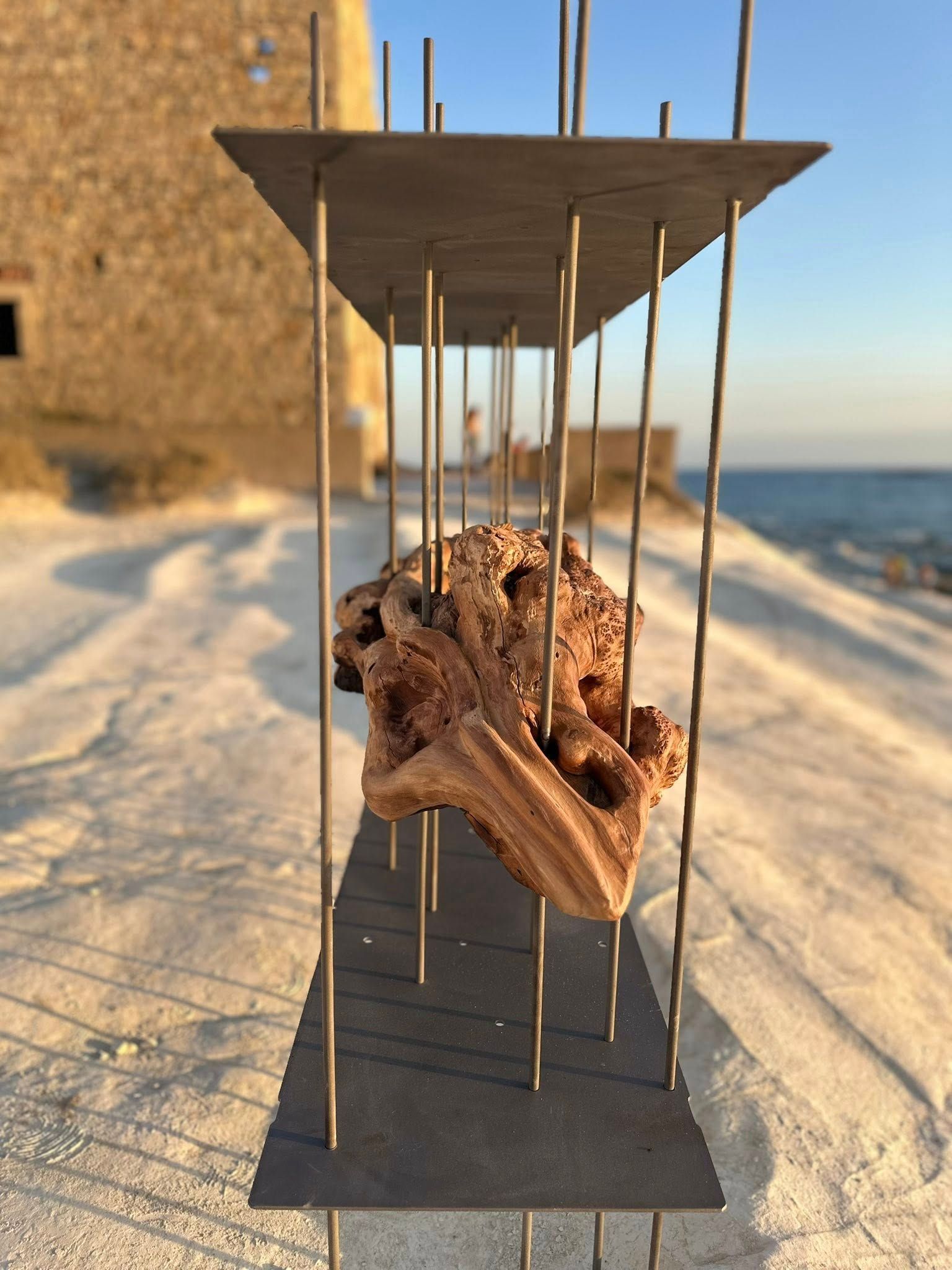 Scultura di una roccia racchiusa in una cornice di metallo su una spiaggia sabbiosa.
