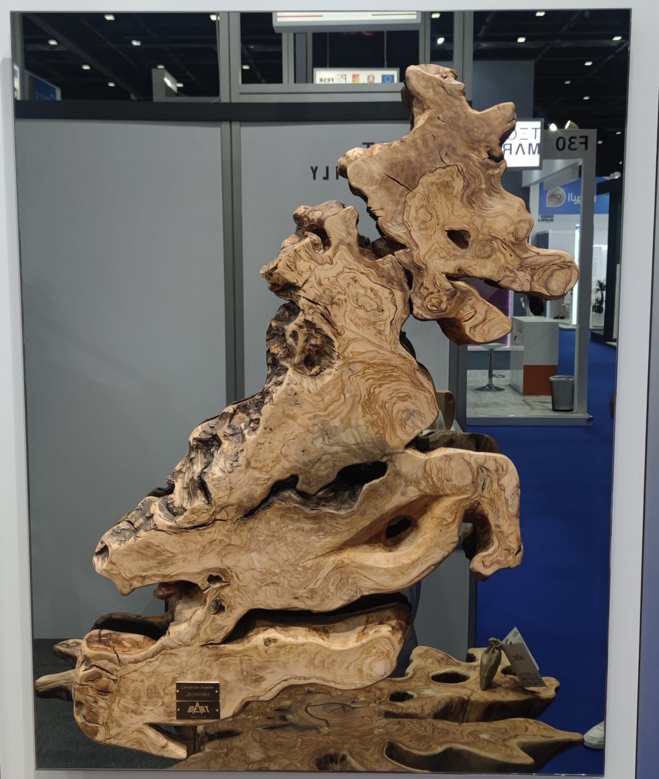 Scultura astratta in legno di colore marrone chiaro, esposta in una fiera.