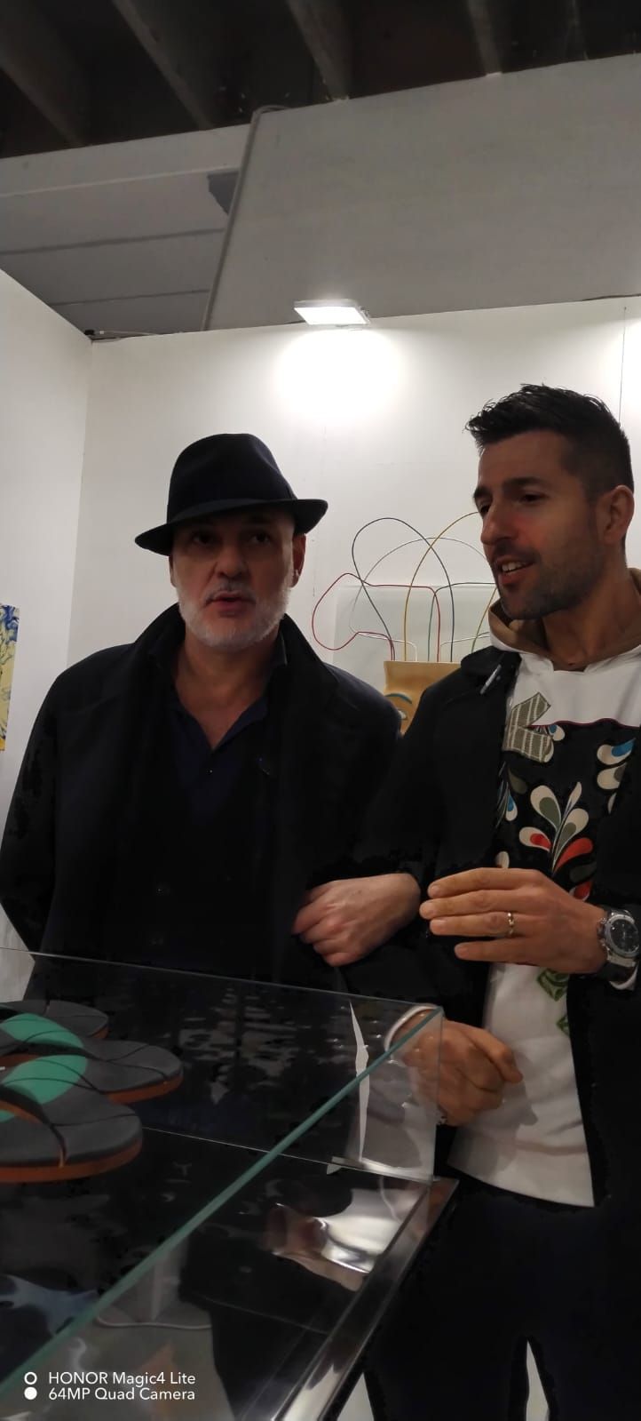 Due uomini in un negozio: uno con un fedora nero e un cappotto, l'altro con una felpa a fiori.