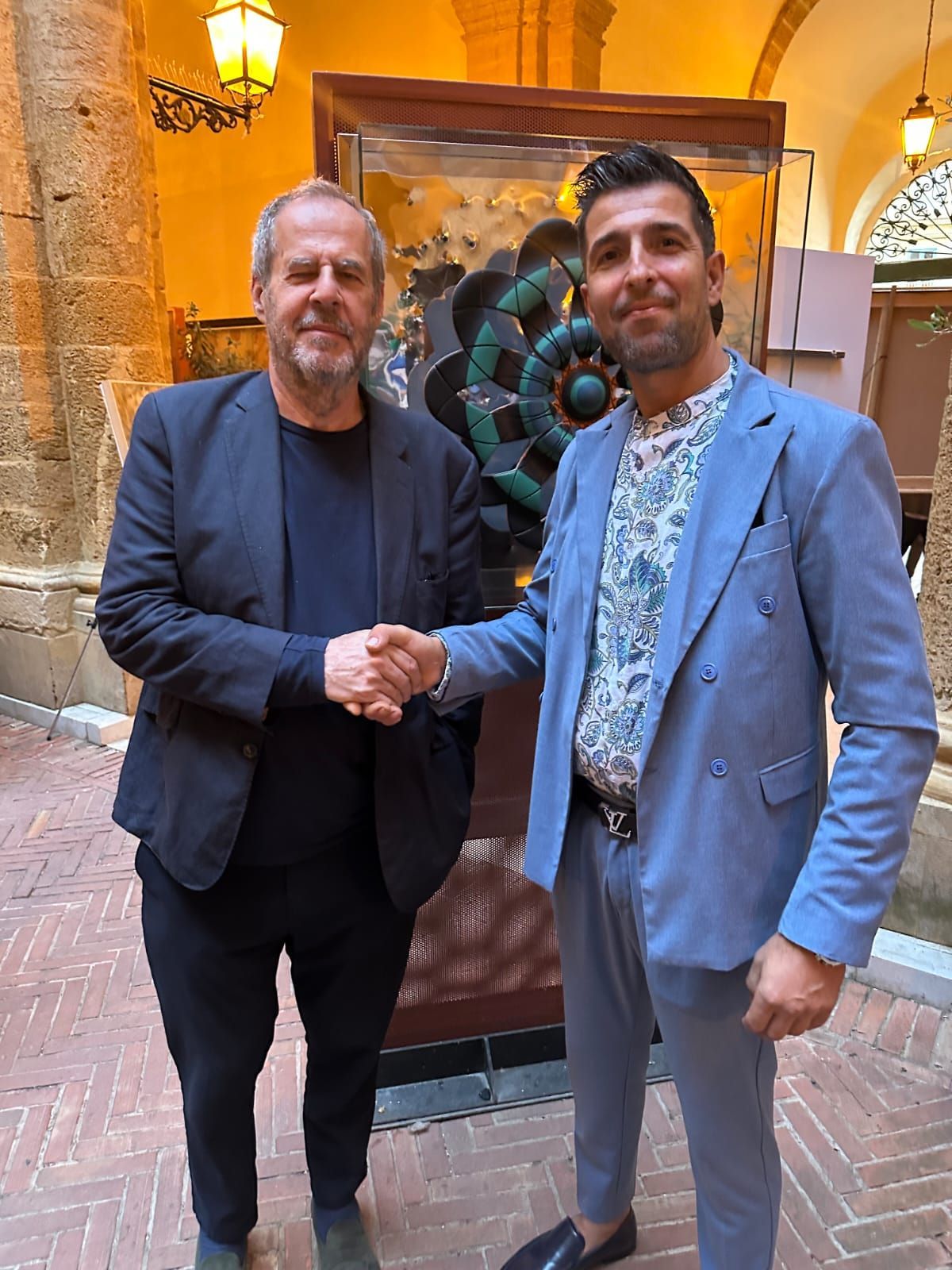 Due uomini in giacca e cravatta si stringono la mano in un ambiente interno decorato.