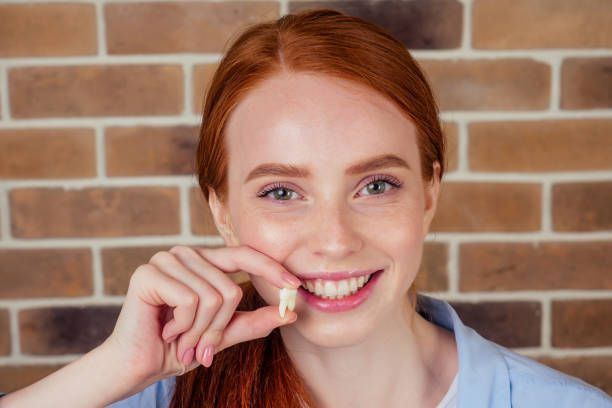 A woman is holding a tooth in her hand in front of a brick wall.