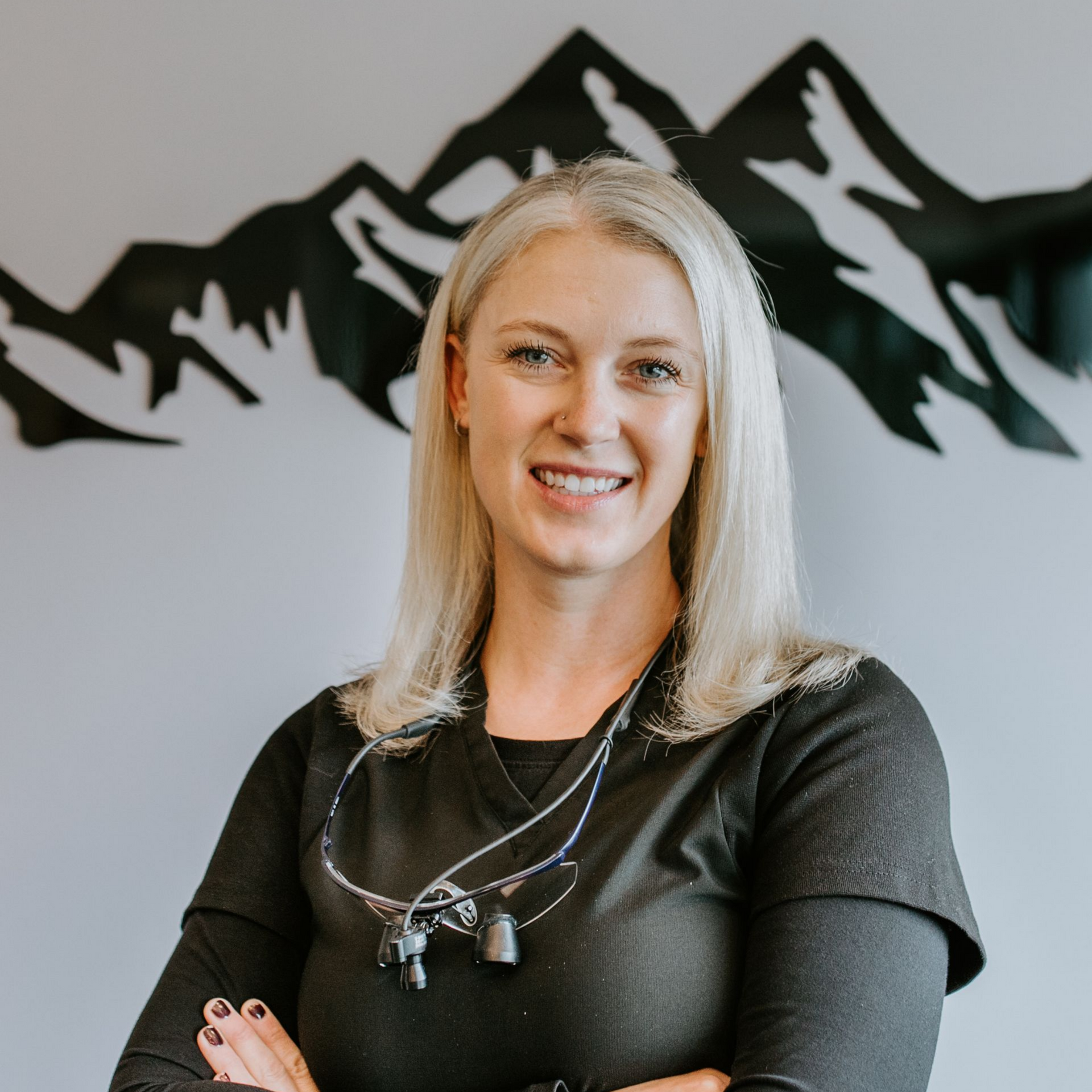 A woman in a black shirt with her arms crossed is smiling.
