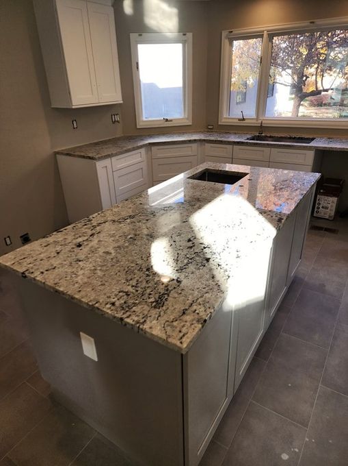Kitchen with granite countertops, island, white cabinets, and windows.