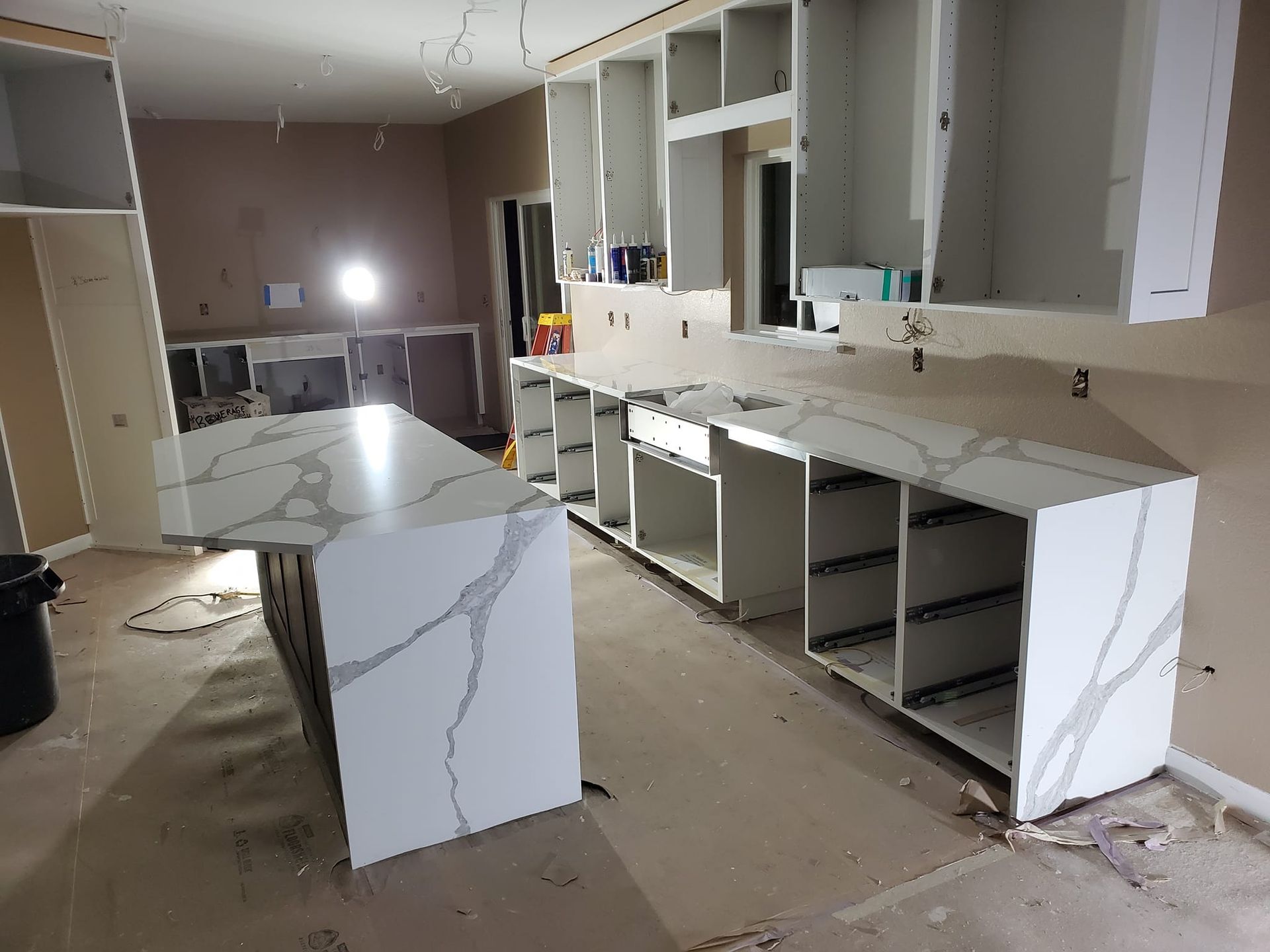 Kitchen renovation in progress: white cabinets and countertops with gray veining, unfinished walls.