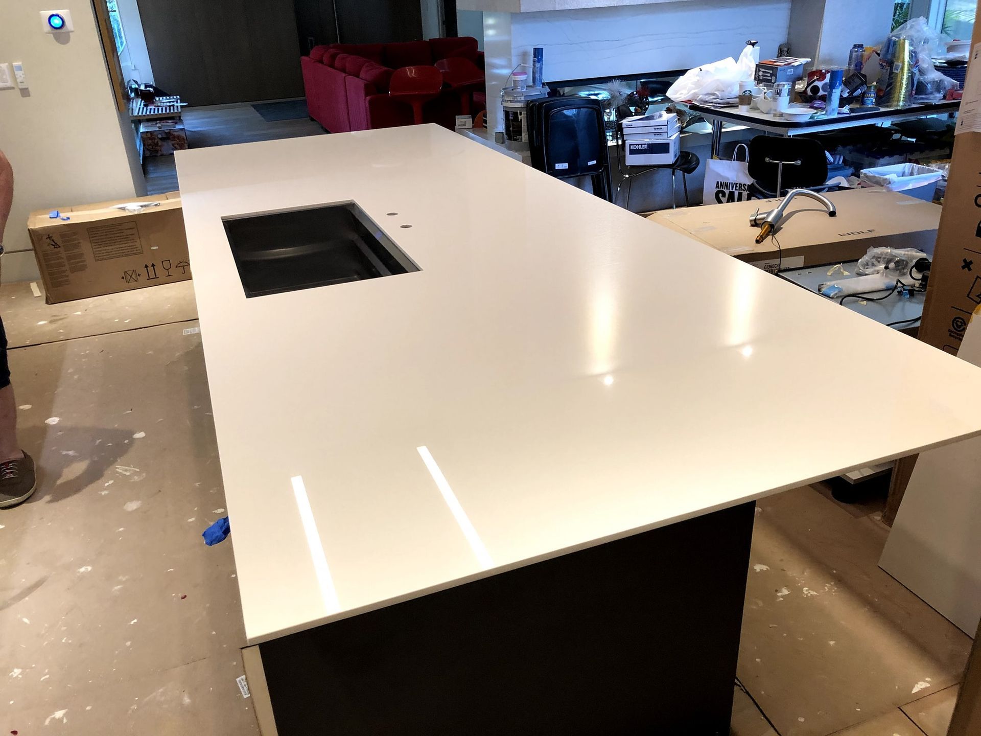White countertop with a black sink, on a dark brown cabinet, in a kitchen.