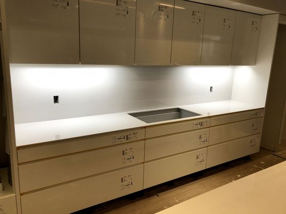 White kitchen cabinets with white countertops and a cooktop. Undercabinet lighting is on.