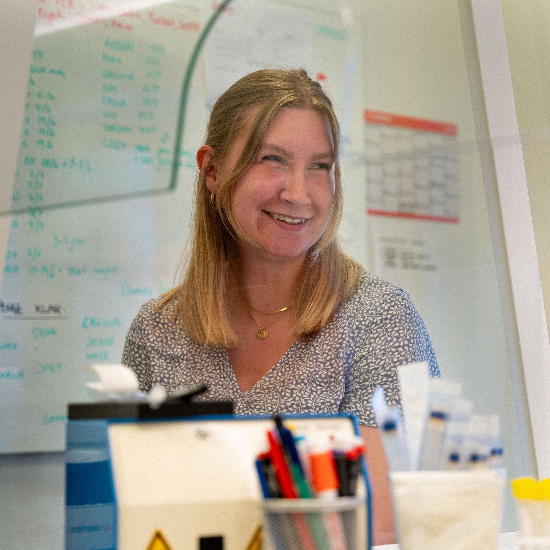 Eine Frau lächelt, während sie vor einer weißen Tafel sitzt.