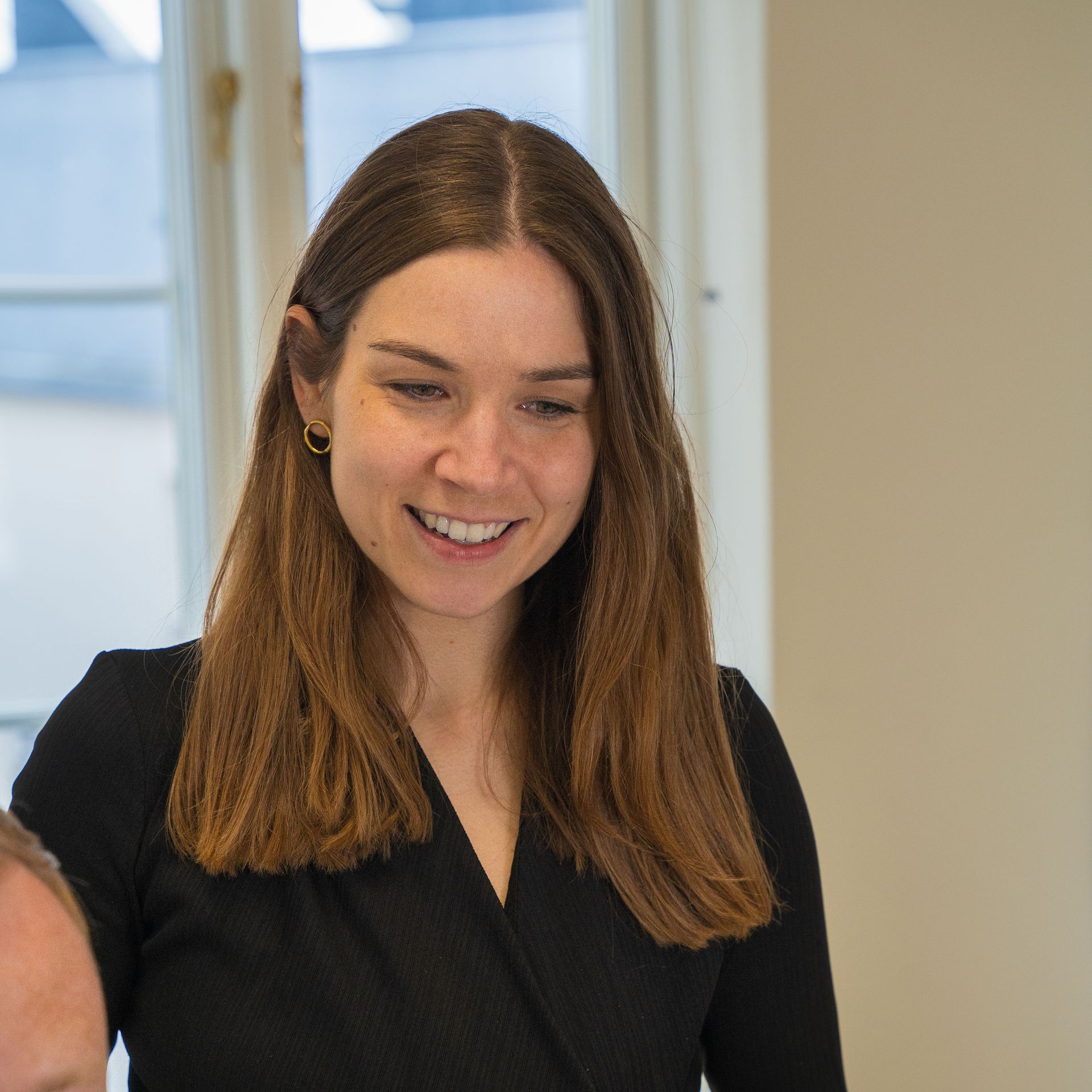 Eine Frau in einem schwarzen Hemd lächelt vor einem Fenster.
