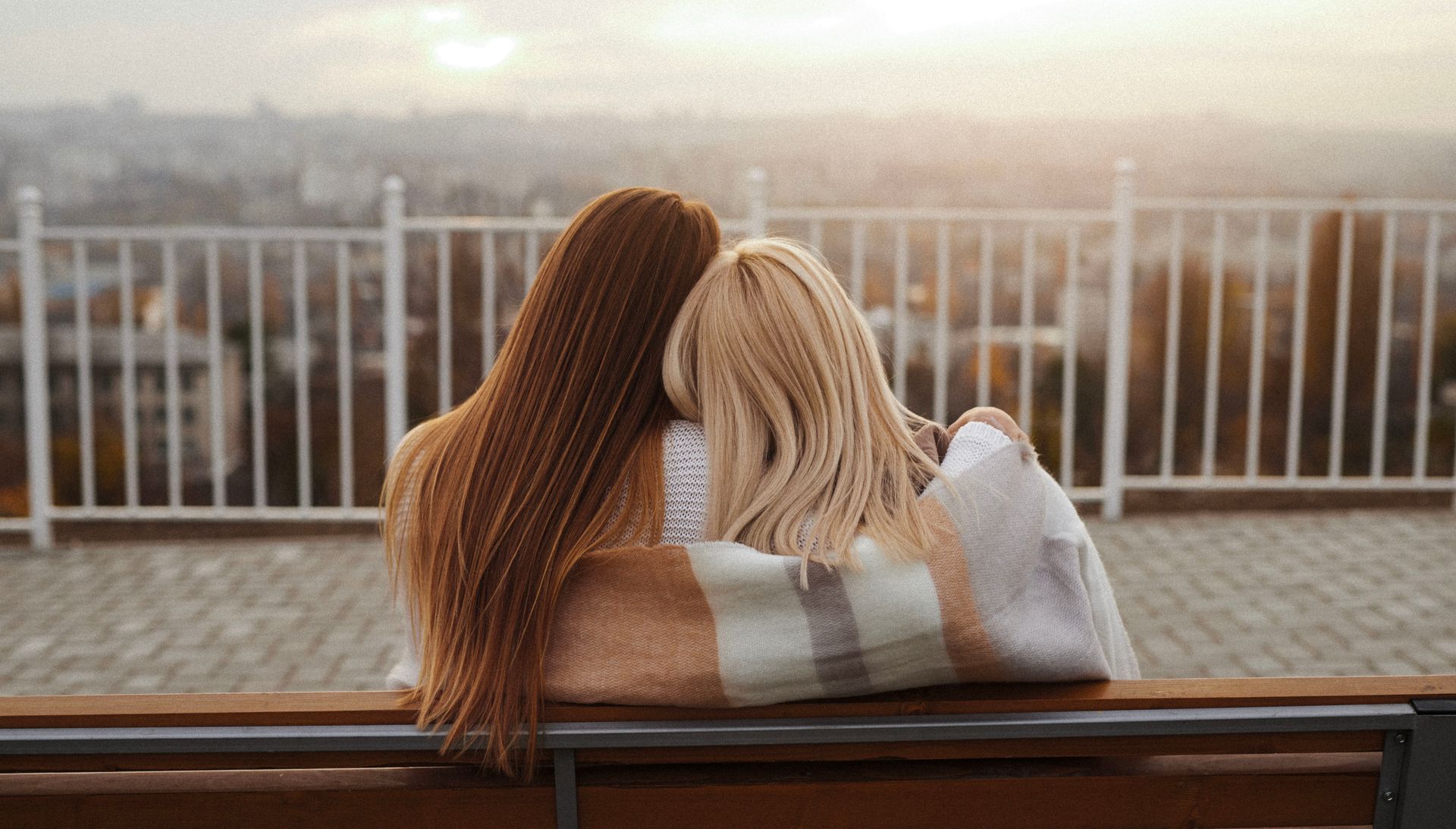 Two women are sitting on a bench hugging each other.