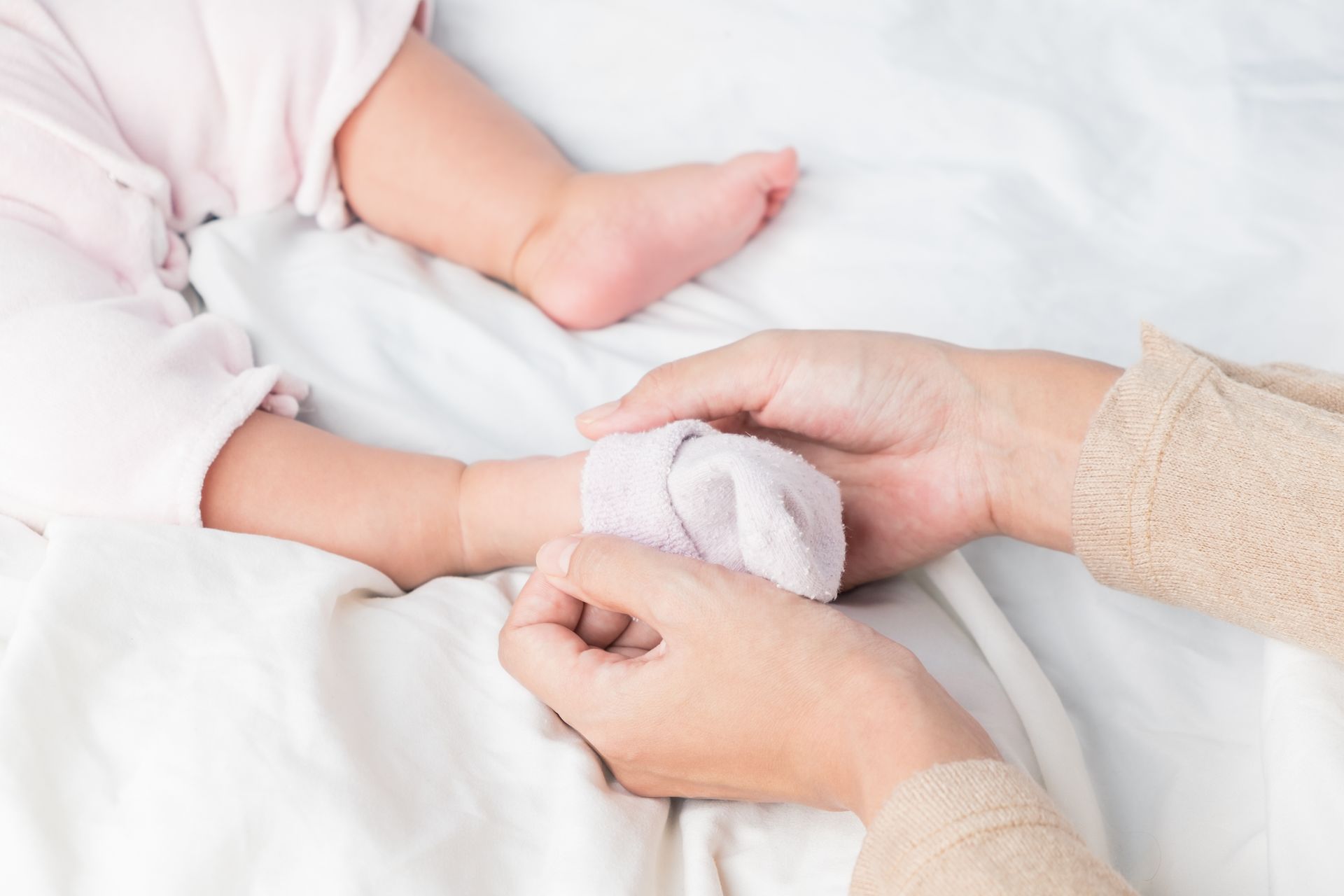 A woman is holding the hand of a baby on a bed.