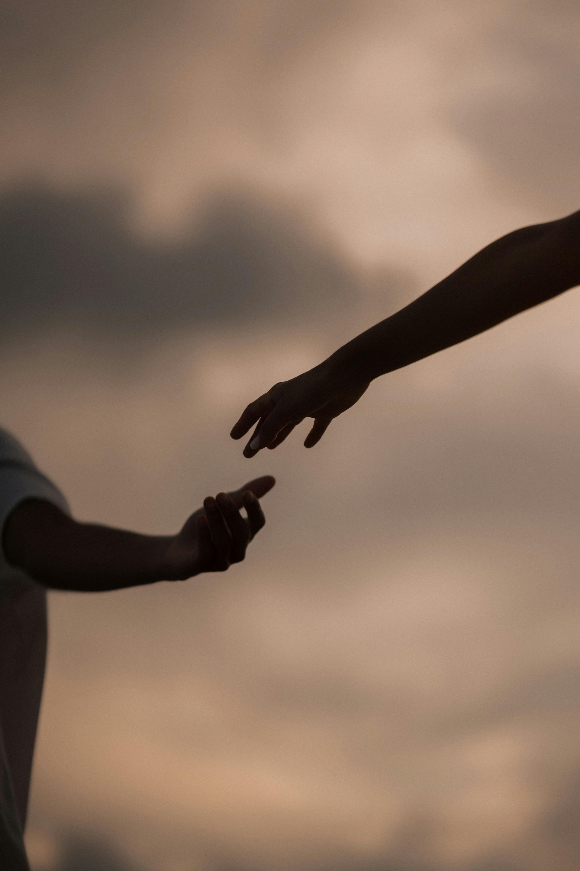 Two hands reaching toward each other against a cloudy sunset sky