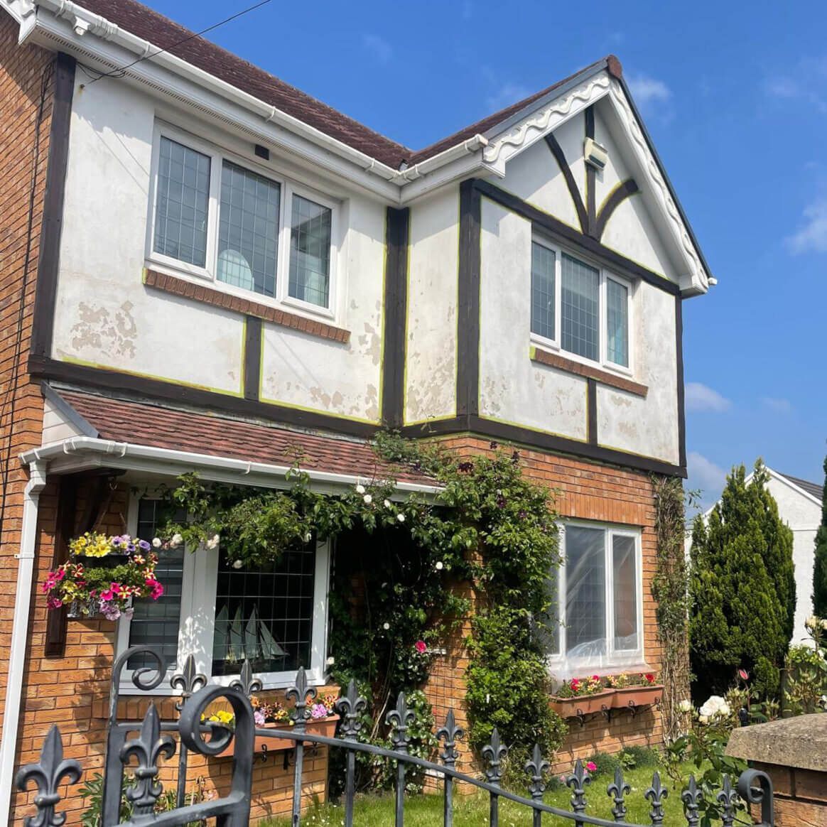 Two-story house with brick base and white, Tudor-style upper facade. Ivy grows around a window, blue sky. Swansea property before refurbishment.