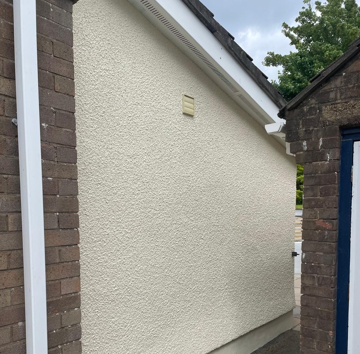 Exterior wall with textured light beige finish, adjacent to a brick wall.