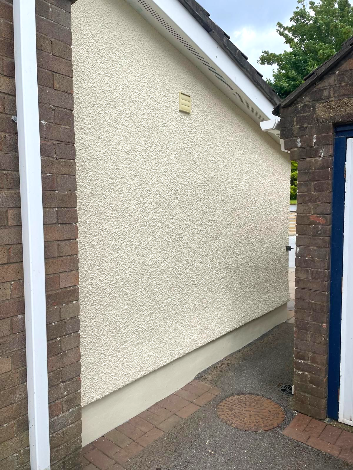 Side of a building with textured cream-colored stucco wall, brick edging, and narrow pathway.