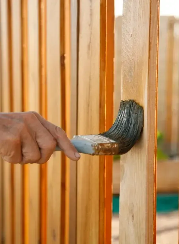 A hand painting a fence wood brown light colour