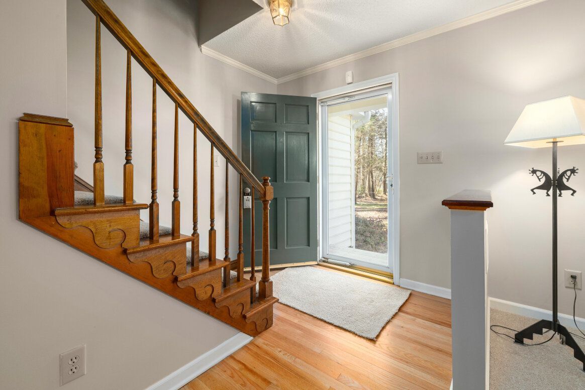 Entryway with wooden staircase, open teal door, and floor lamp.