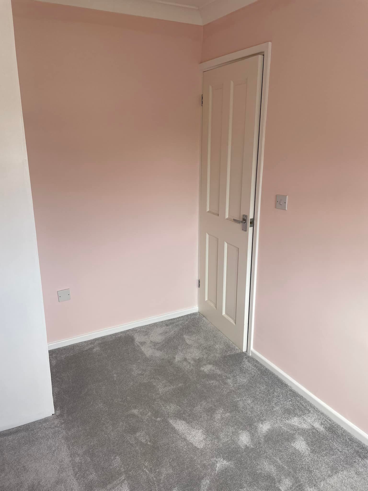 An empty room with pink walls and a gray carpet.
