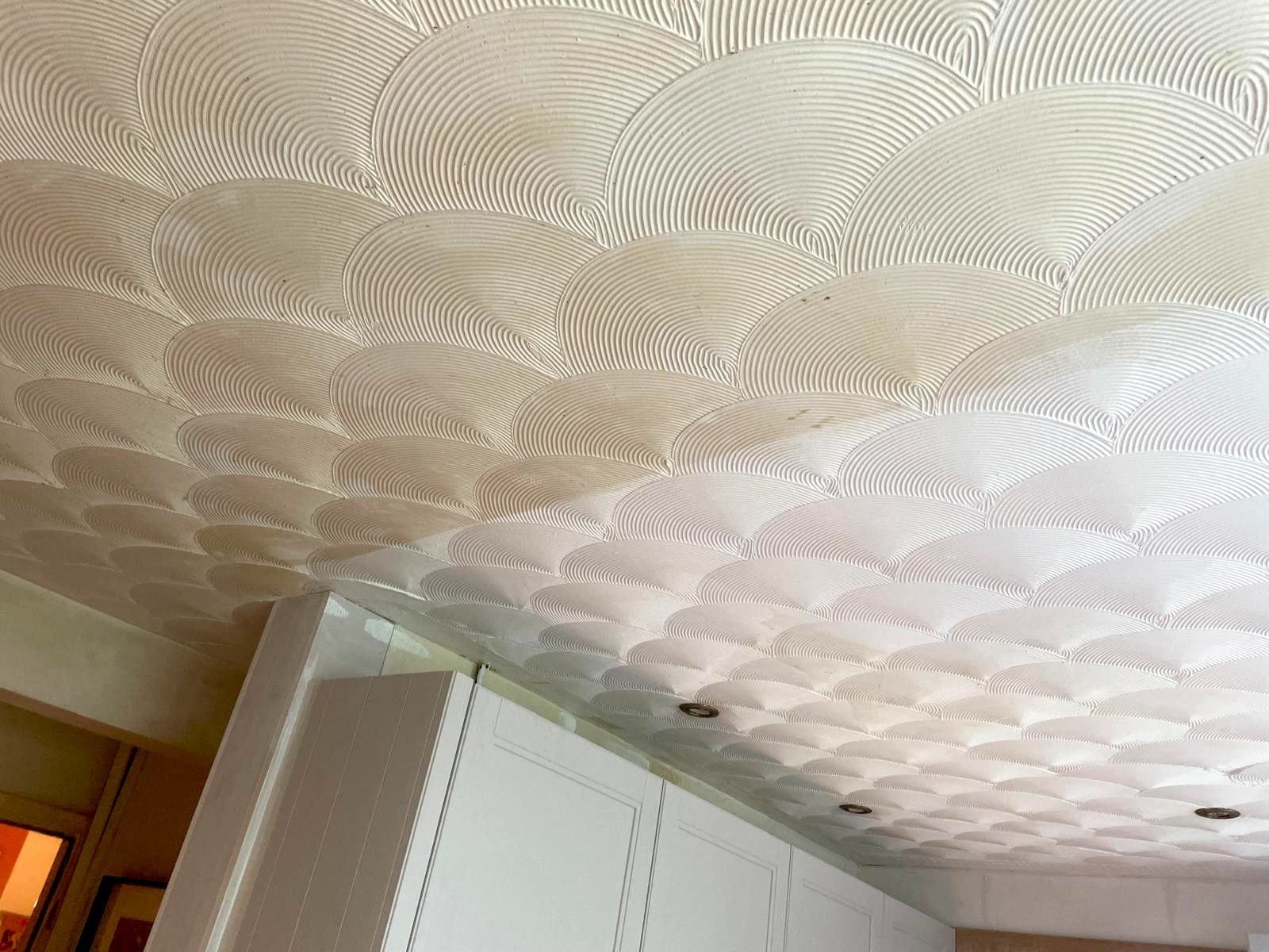 White textured ceiling with a repeating scallop pattern over white cabinets.