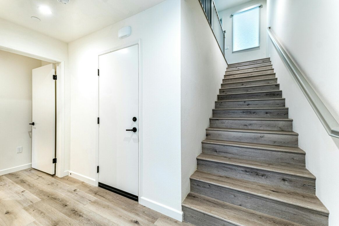 Hallway with stairs and white doors, wood-look flooring. Staircase leads up to a window.