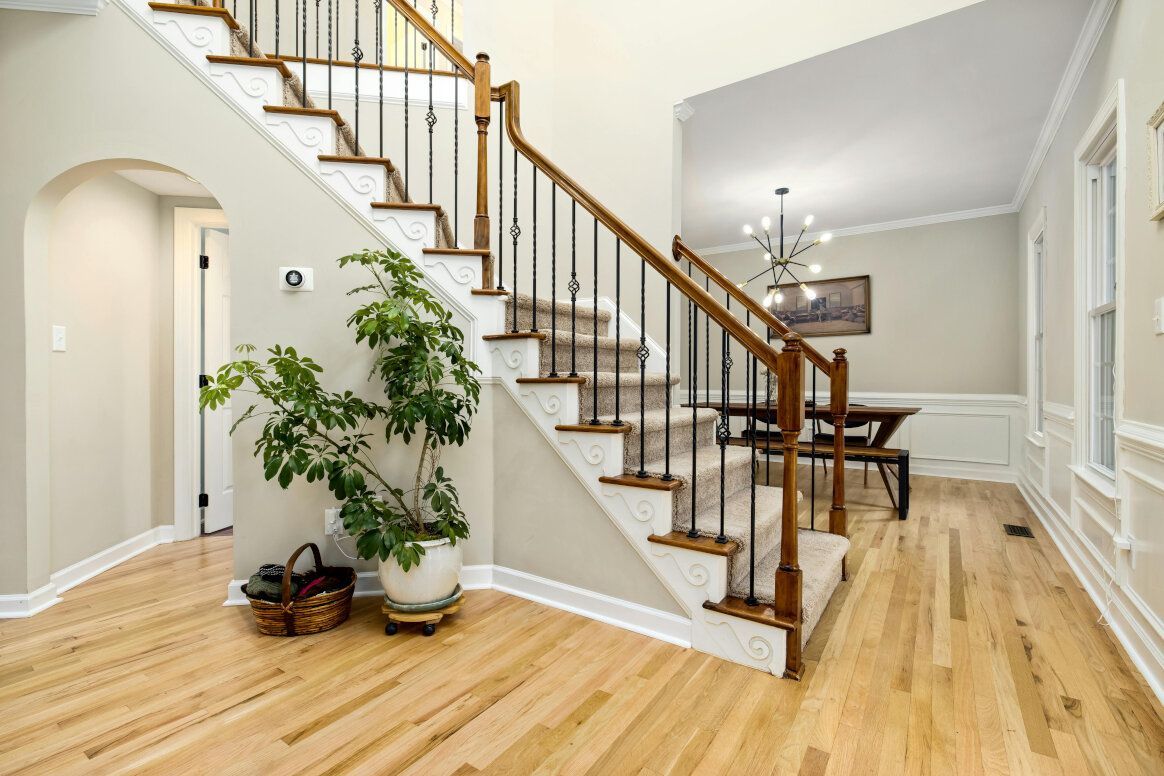 A bright entryway with stairs, wooden floors, and a dining room in the background.