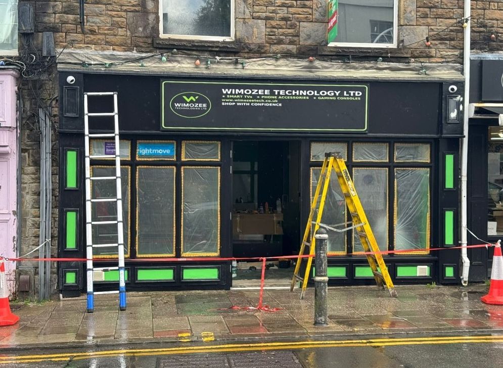 Shopfront with a ladder and scaffolding being renovated; black, green, and gold trim.