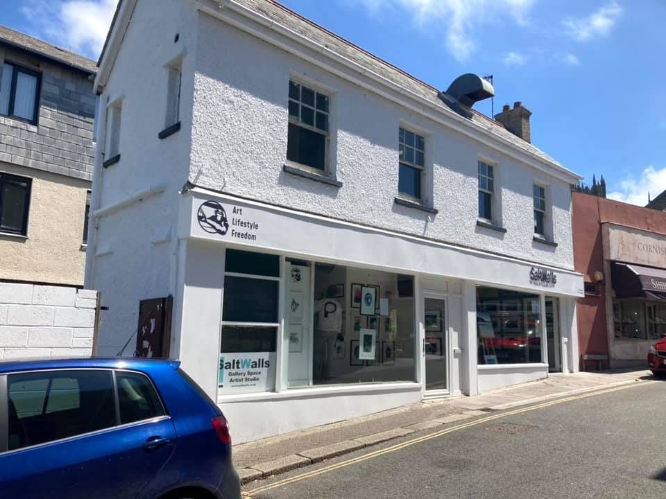 White two-story building with a gallery storefront on a sunny street, blue car parked in foreground.