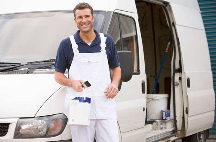 A man in white overalls is standing in front of a white van.