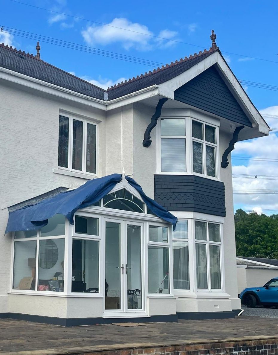 Two-story white house with blue accents, white windows, and a glass-enclosed porch. Blue tarp on the porch roof.
