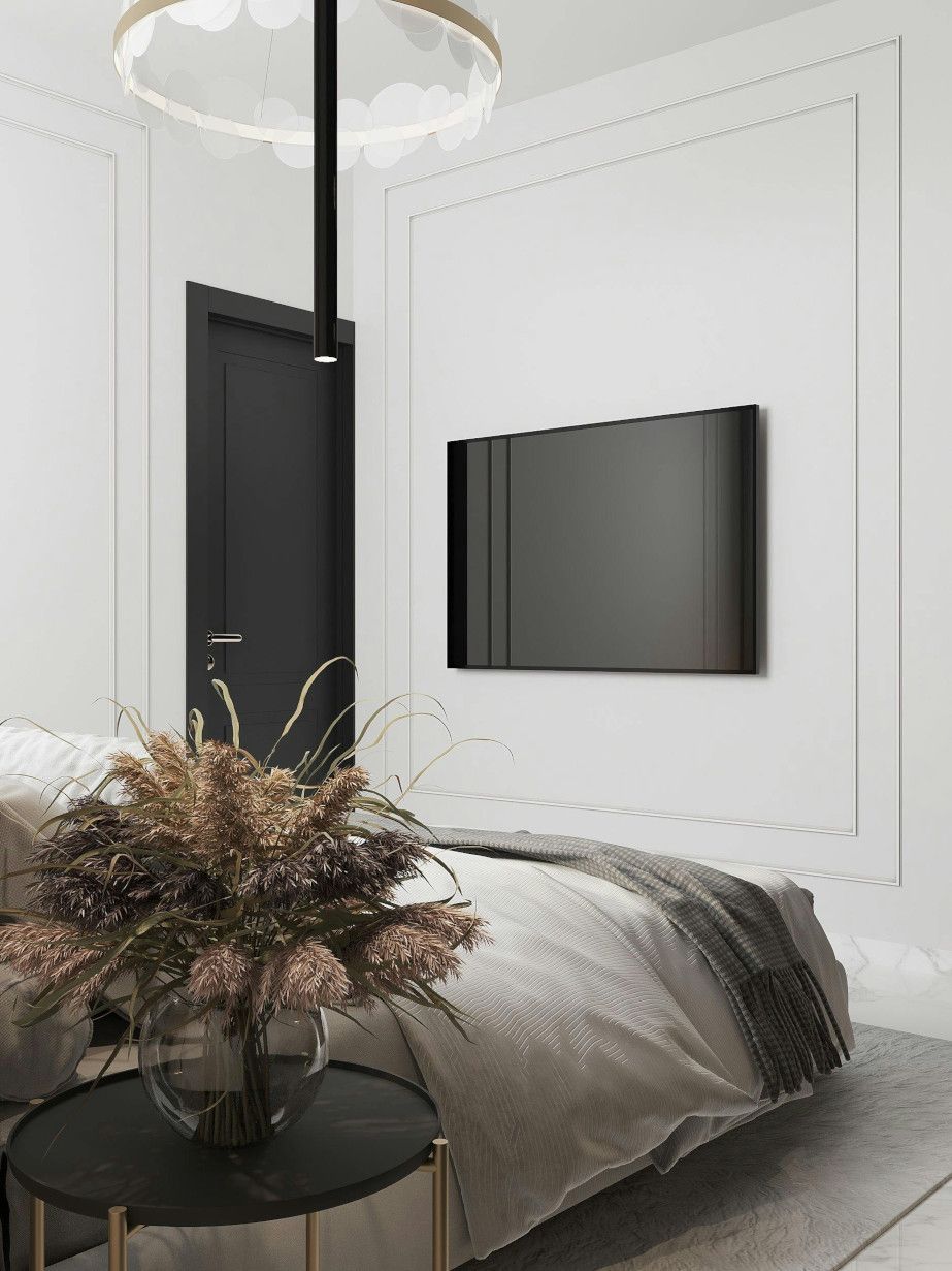 A bedroom with a bed , table , television and a vase of flowers.