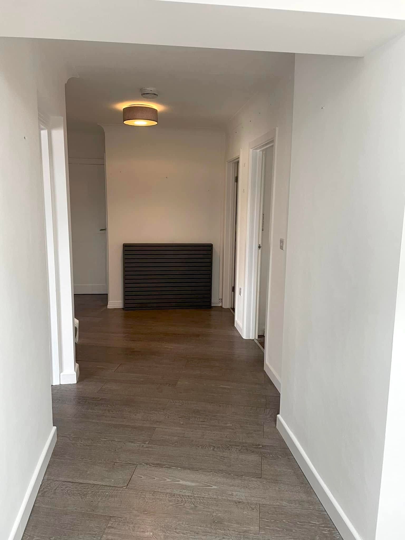A long hallway with white walls and a brown floor leading to a room.