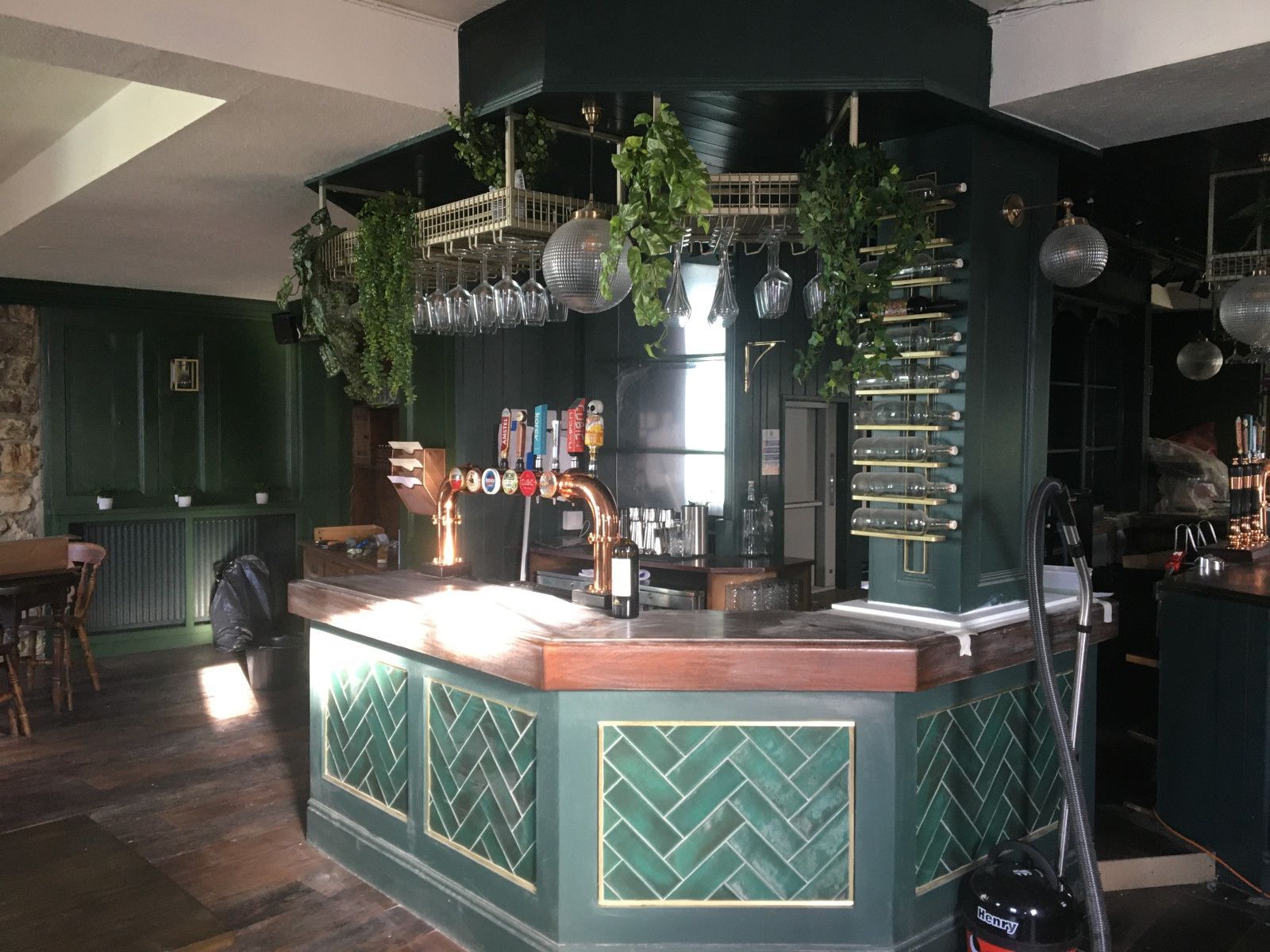 A bar in a restaurant with green tiles and a vacuum cleaner.