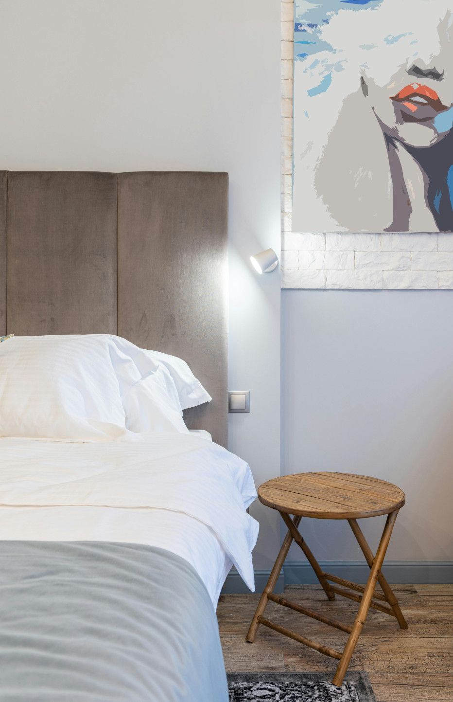A bedroom with a bed , stool and a painting on the wall.