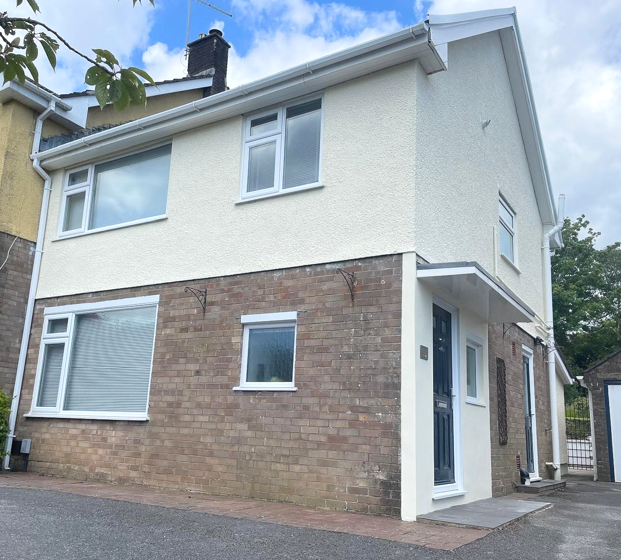 Two-story house with cream stucco upper half and brick lower half; windows with white trim; cloudy sky.